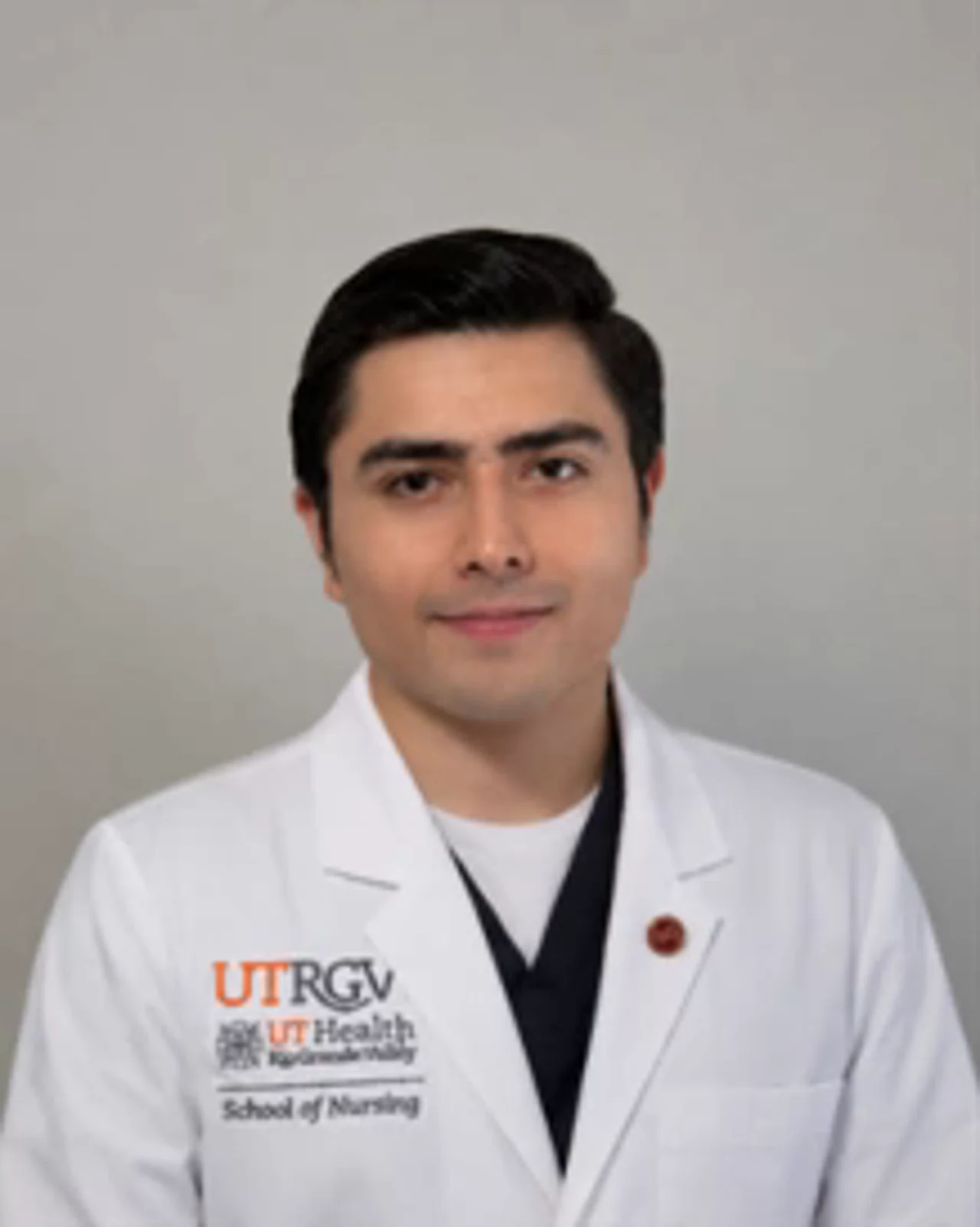 Portrait of Francisco Nunez wearing a white UTRGV School of Nursing lab coat, facing the camera against a light background.