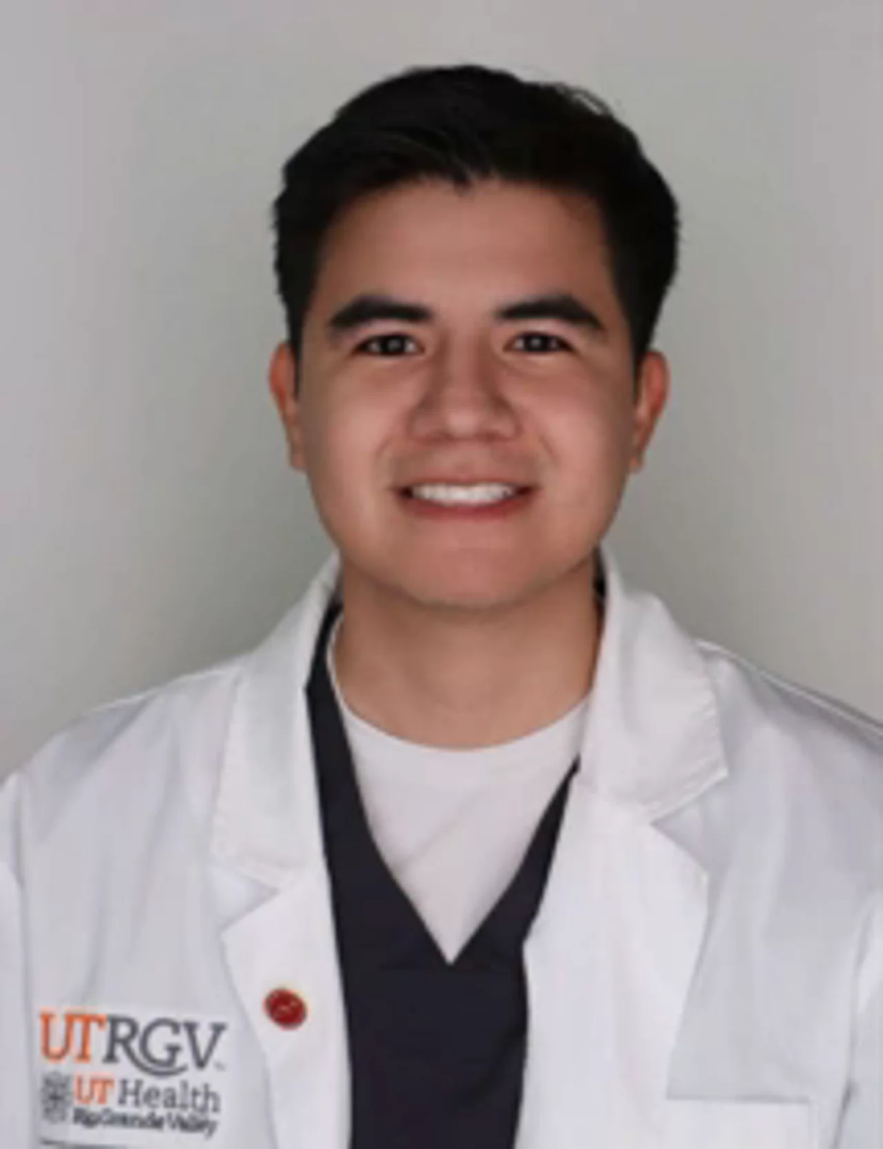 Portrait of Jacob J. Perez wearing a white UTRGV School of Nursing lab coat, facing the camera with a smile against a plain background.