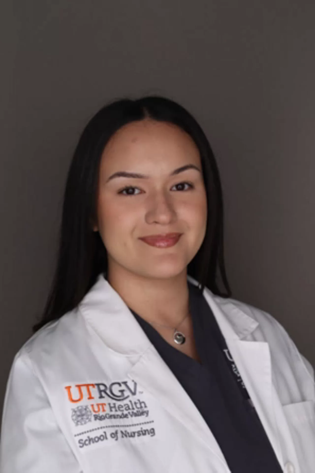 Portrait of Joselyne Salinas wearing a white UTRGV School of Nursing lab coat, facing the camera against a neutral background.