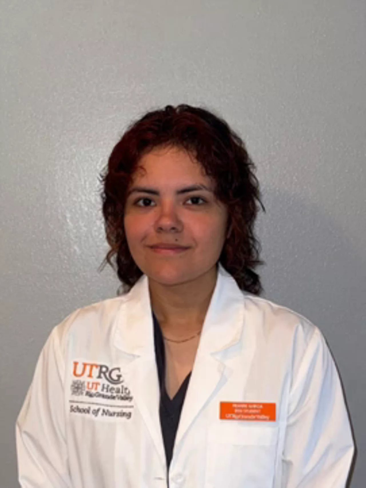 Portrait of Reanne Garcia wearing a white UTRGV School of Nursing lab coat, facing the camera against a neutral background.