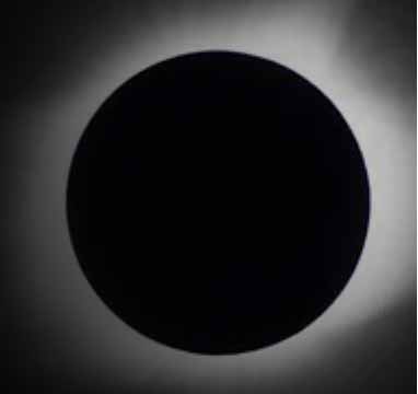 A total solar eclipse showing the dark silhouette of the moon completely covering the sun, with the sun’s corona forming a glowing ring around the edges.