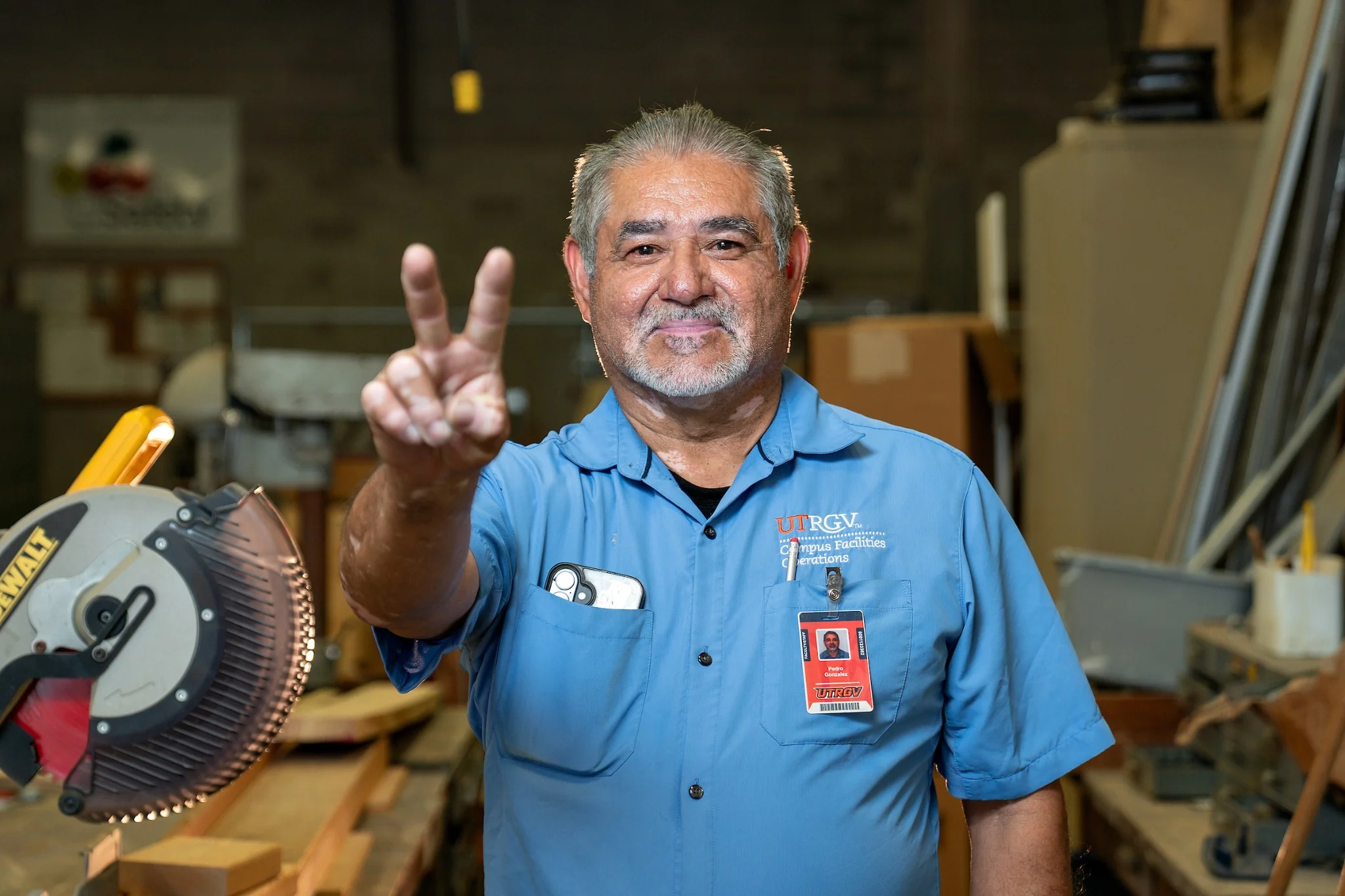 UTRGV Campus Facilities Operations employee smiles and displays the V hand sign in a workshop.