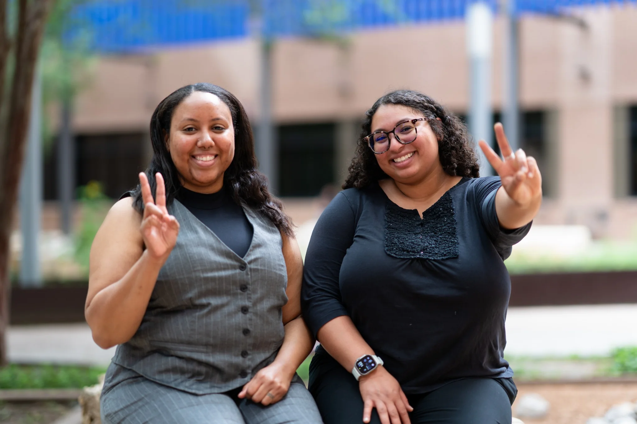 Two UTRGV employees smile and display the V hand sign outdoors on campus.