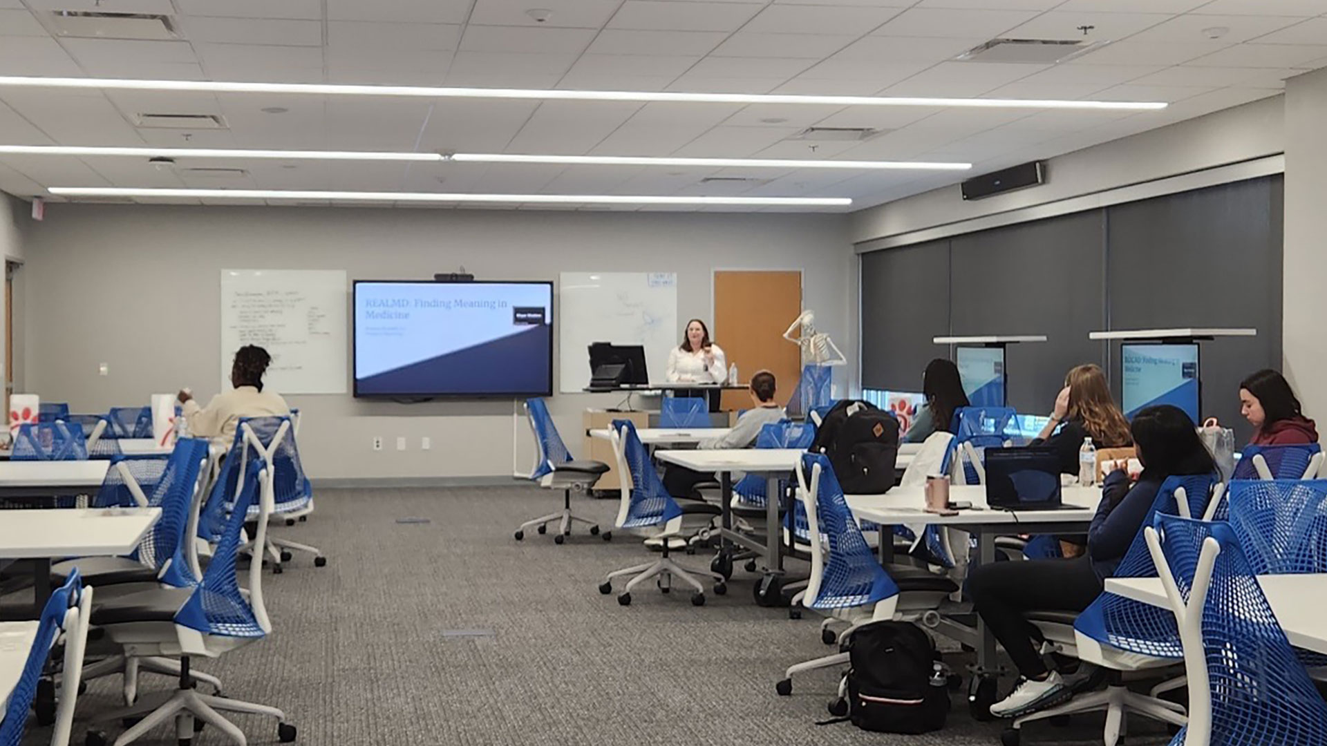 A presentation on "Finding Meaning in Medicine" is being given to a group of students in a modern classroom.