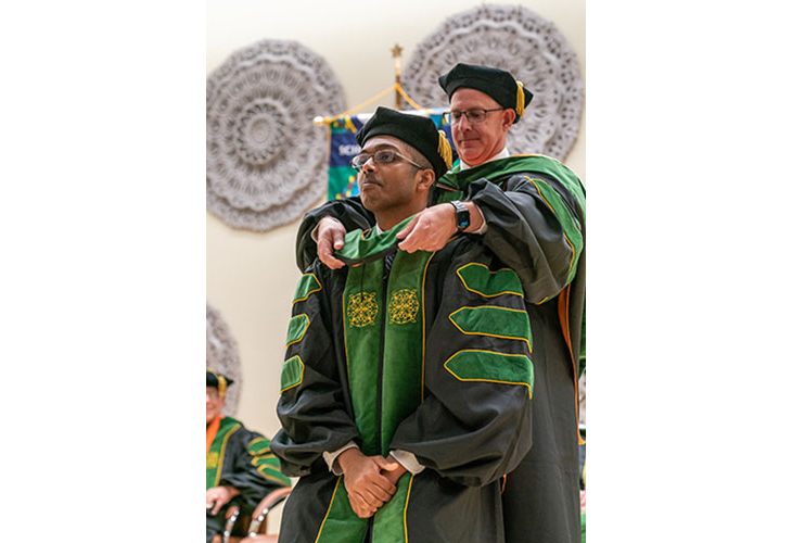 Dr. Jeremy Gibson, Vice Dean of Education, hooding Christian Thomas Abraham. Page Banner 