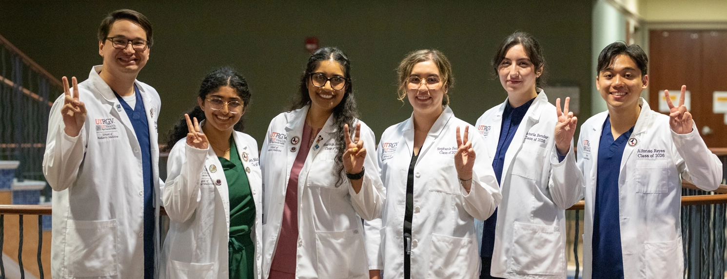 SOPM students in white coats signaling v's up.