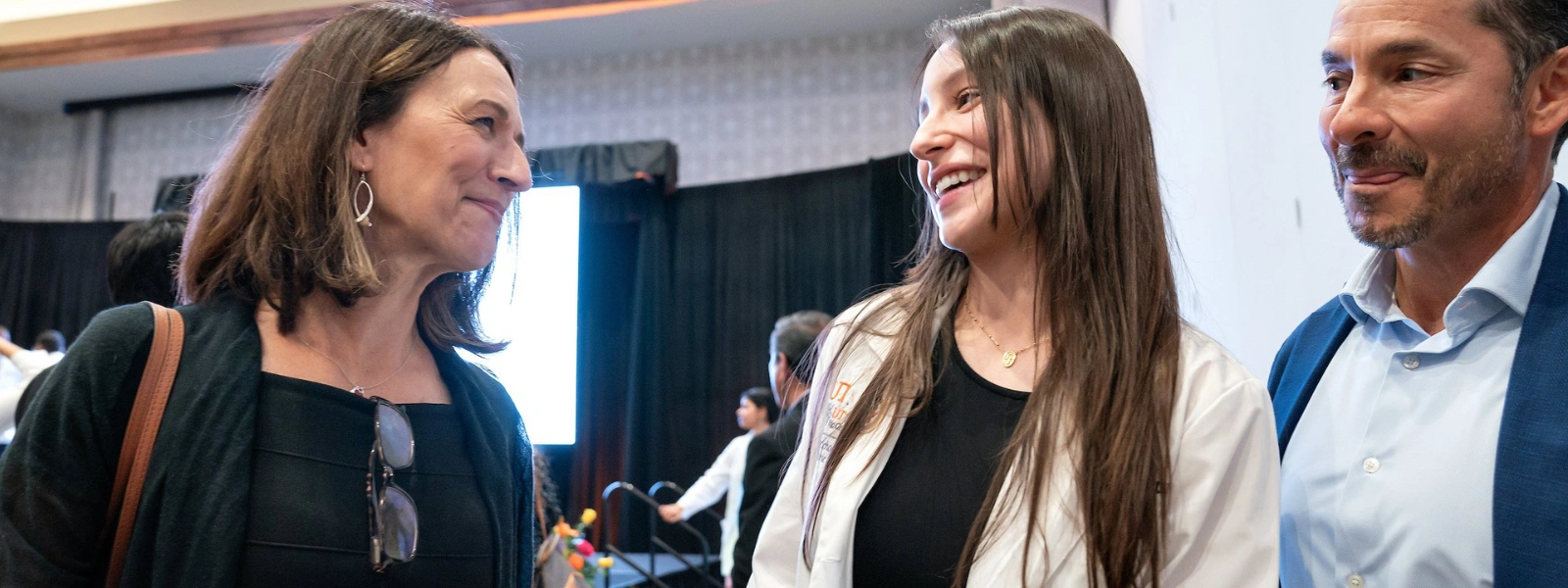 SOPM student with parents on stage during event.