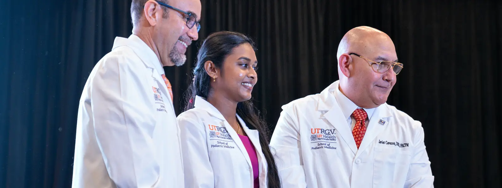 Student with dean and faculty during white coat ceremony.
