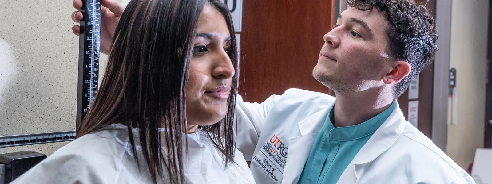 SOPM student in white coat measuring a patient's height.