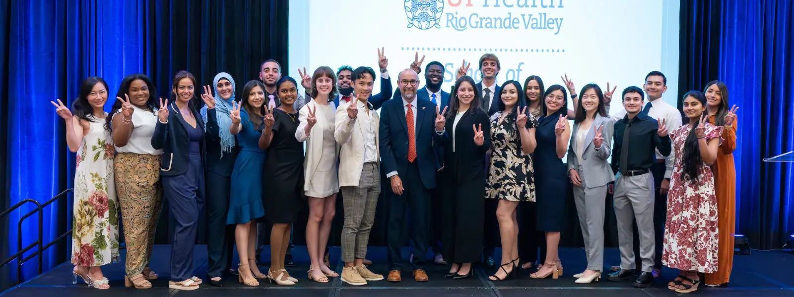 Dean, faculty, and students standing together onstage, posing for a group photo during an event.