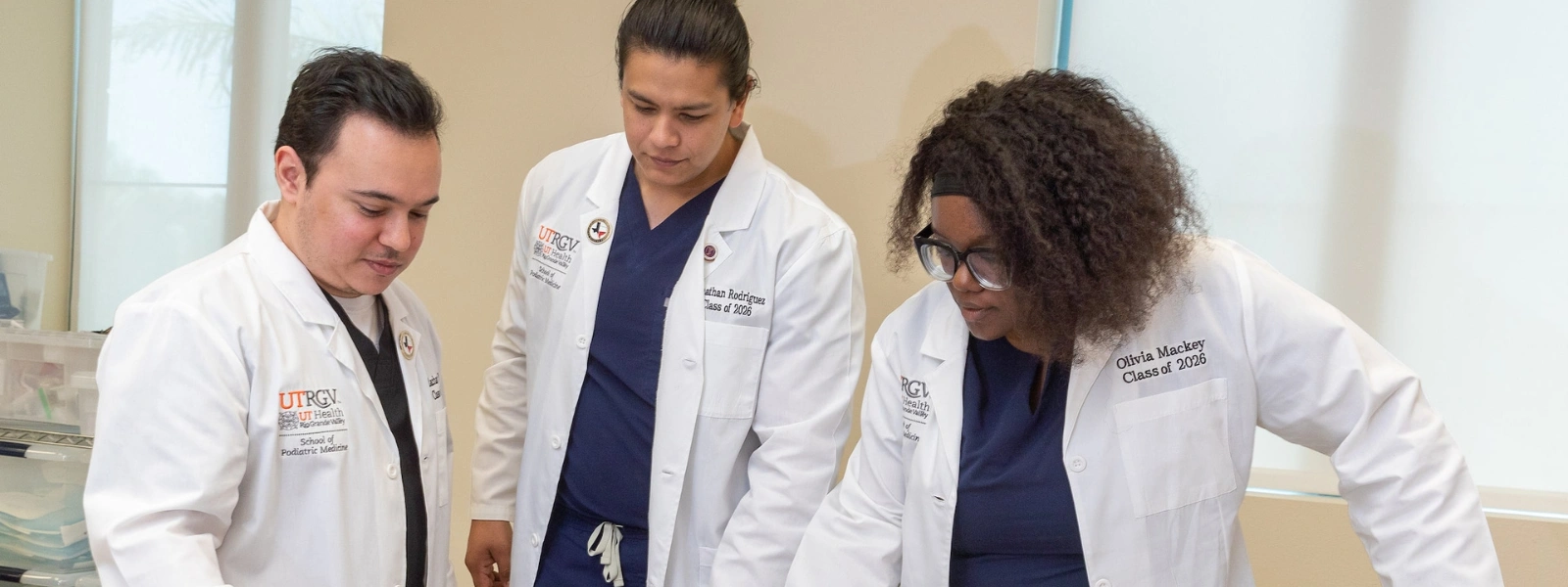 SOPM students practicing clinical skills on a medical manikin in a hospital bed. 