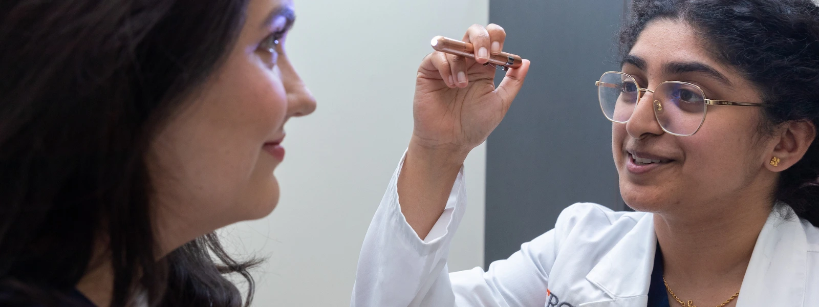 SOPM student looking at patient's eye with small flashlight.