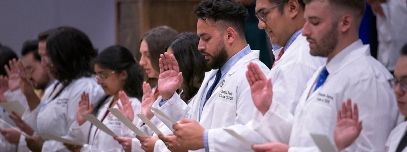 Students raising their right hands to take the oath during the White Coat Ceremony.