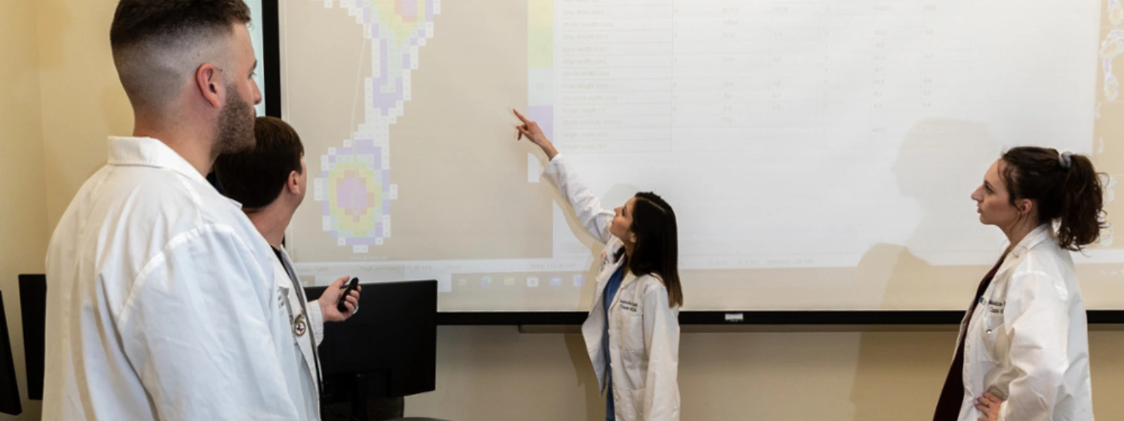 SOPM students gathered around a screen, with one student pointing at it during a collaborative classroom activity. 