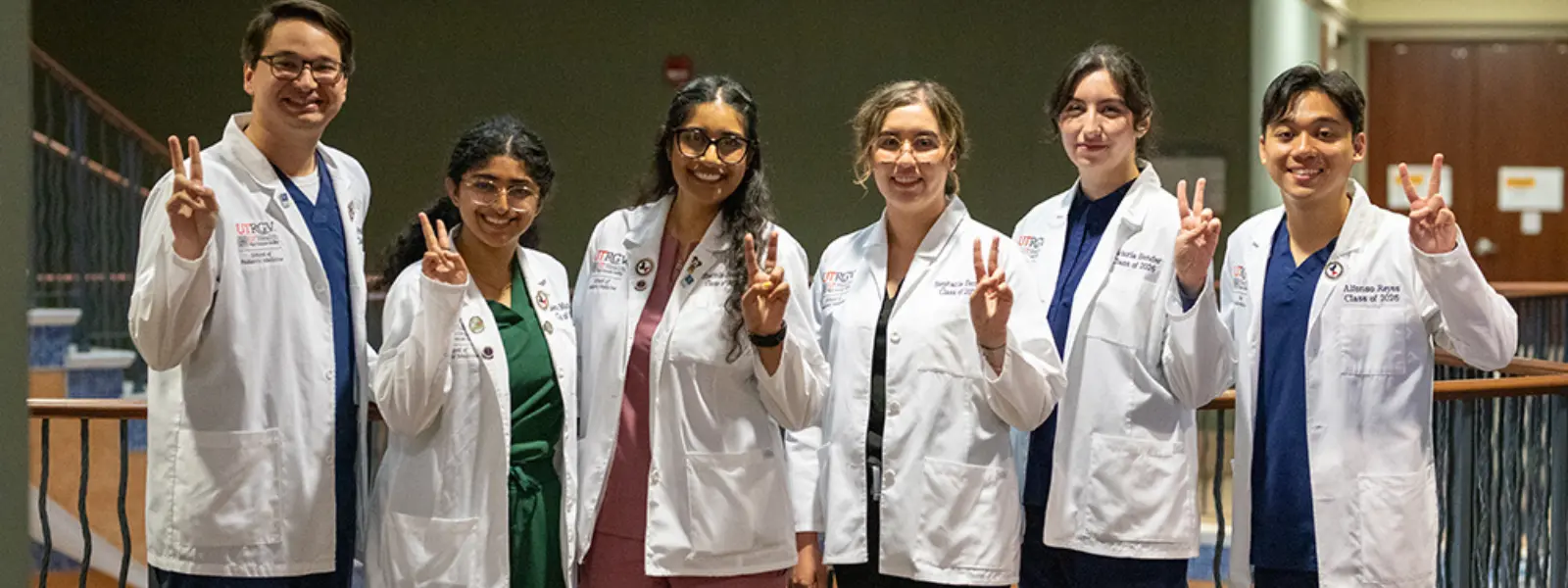 SOPM students wearing white coats making peace signs for a group photo.