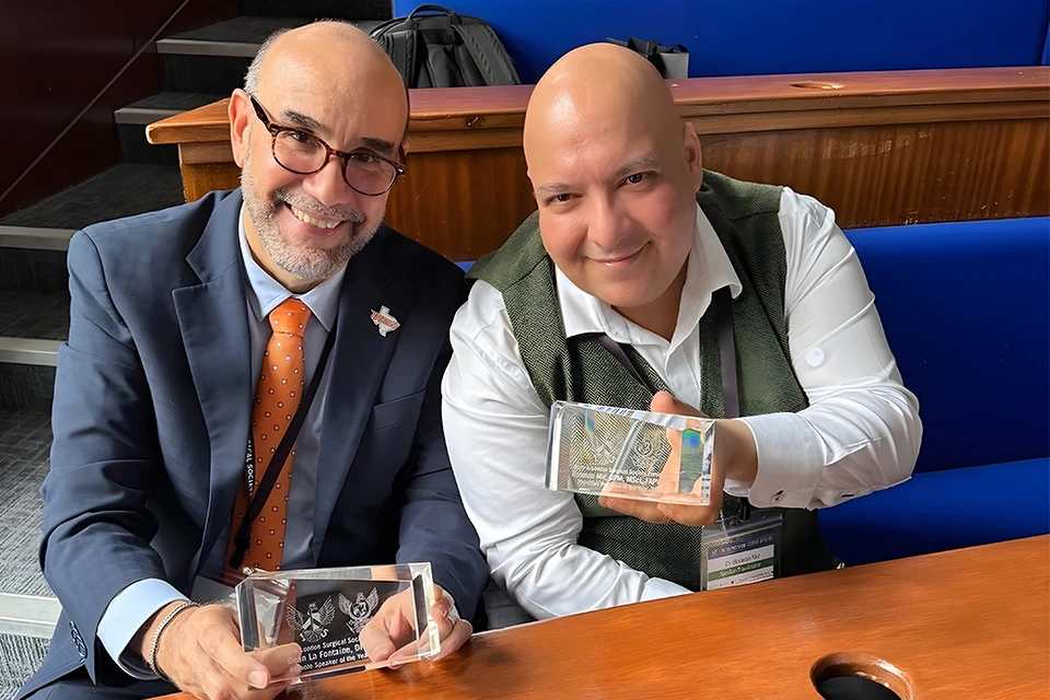 UTRGV dean and faculty member seated at a table smiling while holding award plaques during a recognition event.