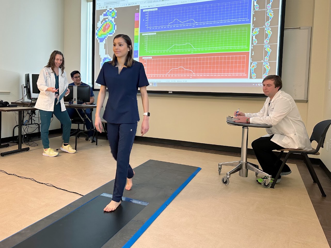 Patient walking while SOPM students in white coats watch.