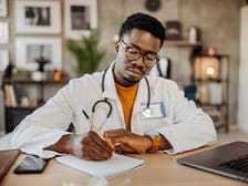 Student wearing a white coat writing notes during a lecture or clinical session.