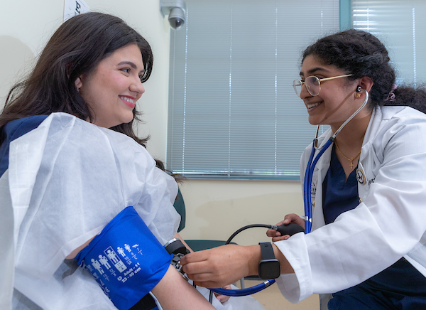 Patient smiles at an SOPM student wearing a white coat while having her blood pressure measured.