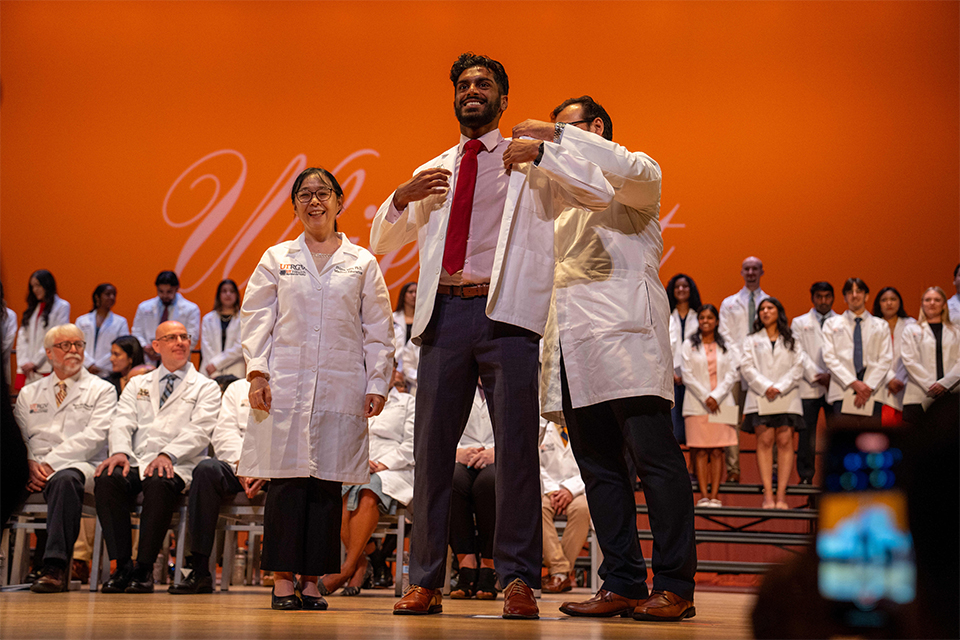 Faculty member helping SOPM student into white coat.