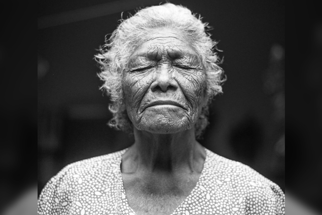 Black and white portrait of an elderly person with their eyes closed.