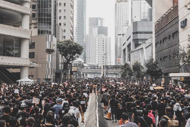 A large crowd of people fills a city street lined with skyscrapers.