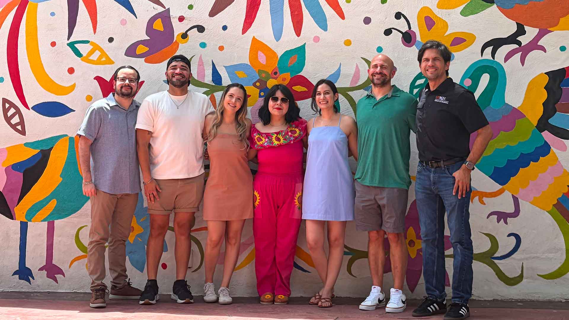 Residents gather for a group portrait in front of a colorful mural during a residency program activity.