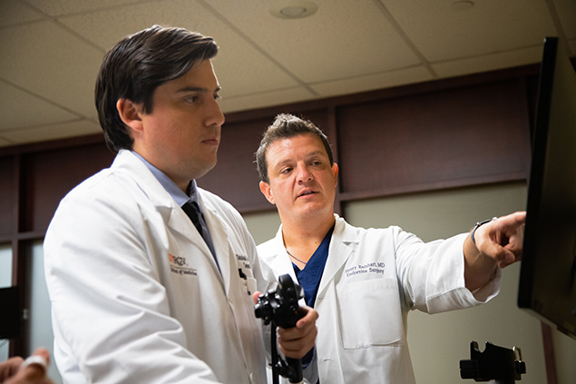 Two doctors in white coats are looking at a computer screen. One is pointing at the screen.  They appear to be discussing a medical image.