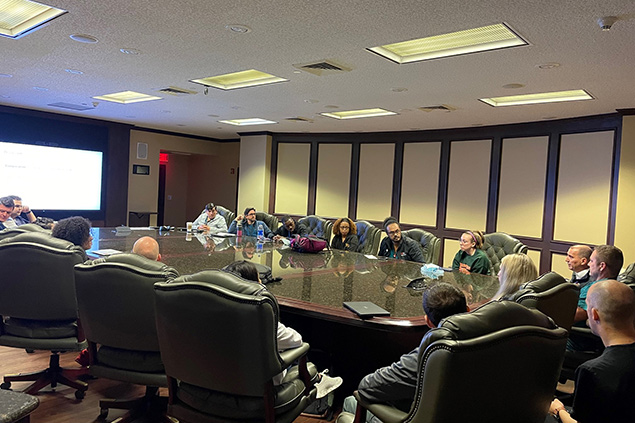 A large group of people sit around a large conference table during a meeting.
