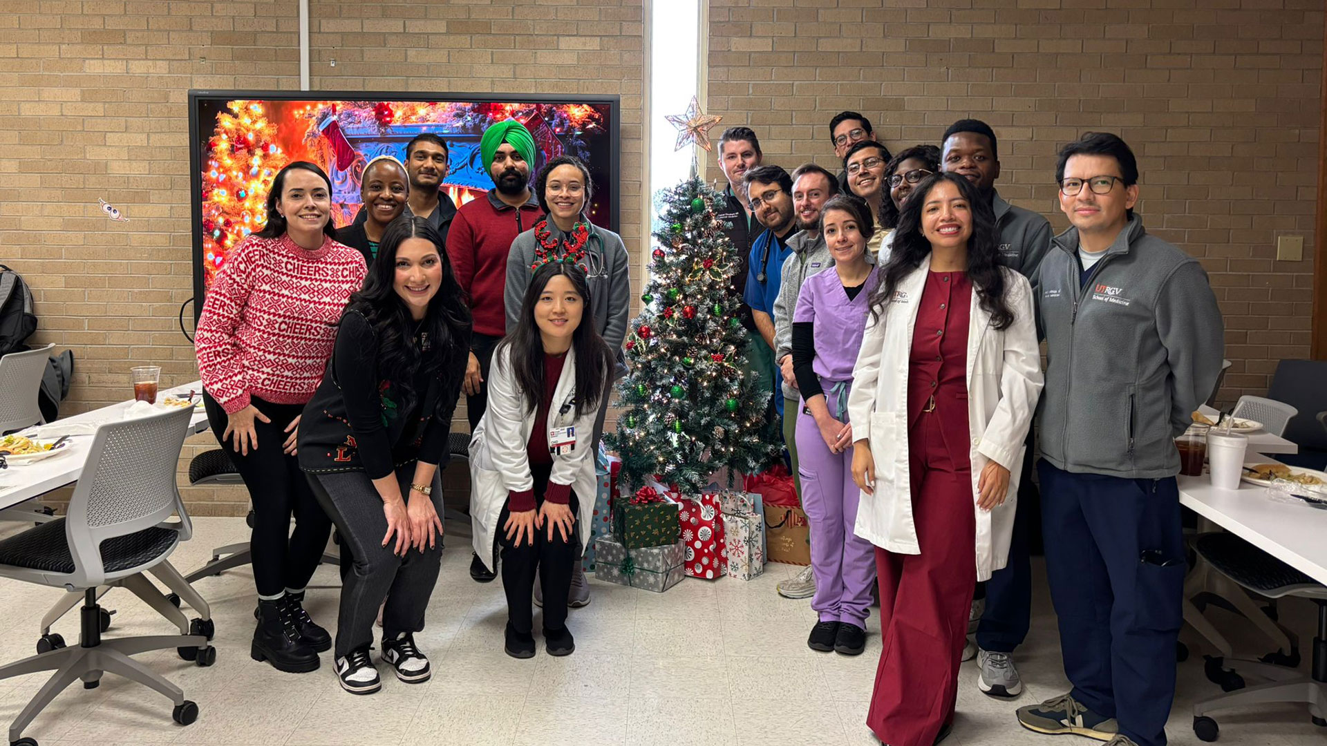 A large group of smiling medical students pose for a photo in front of a decorated Christmas tree.