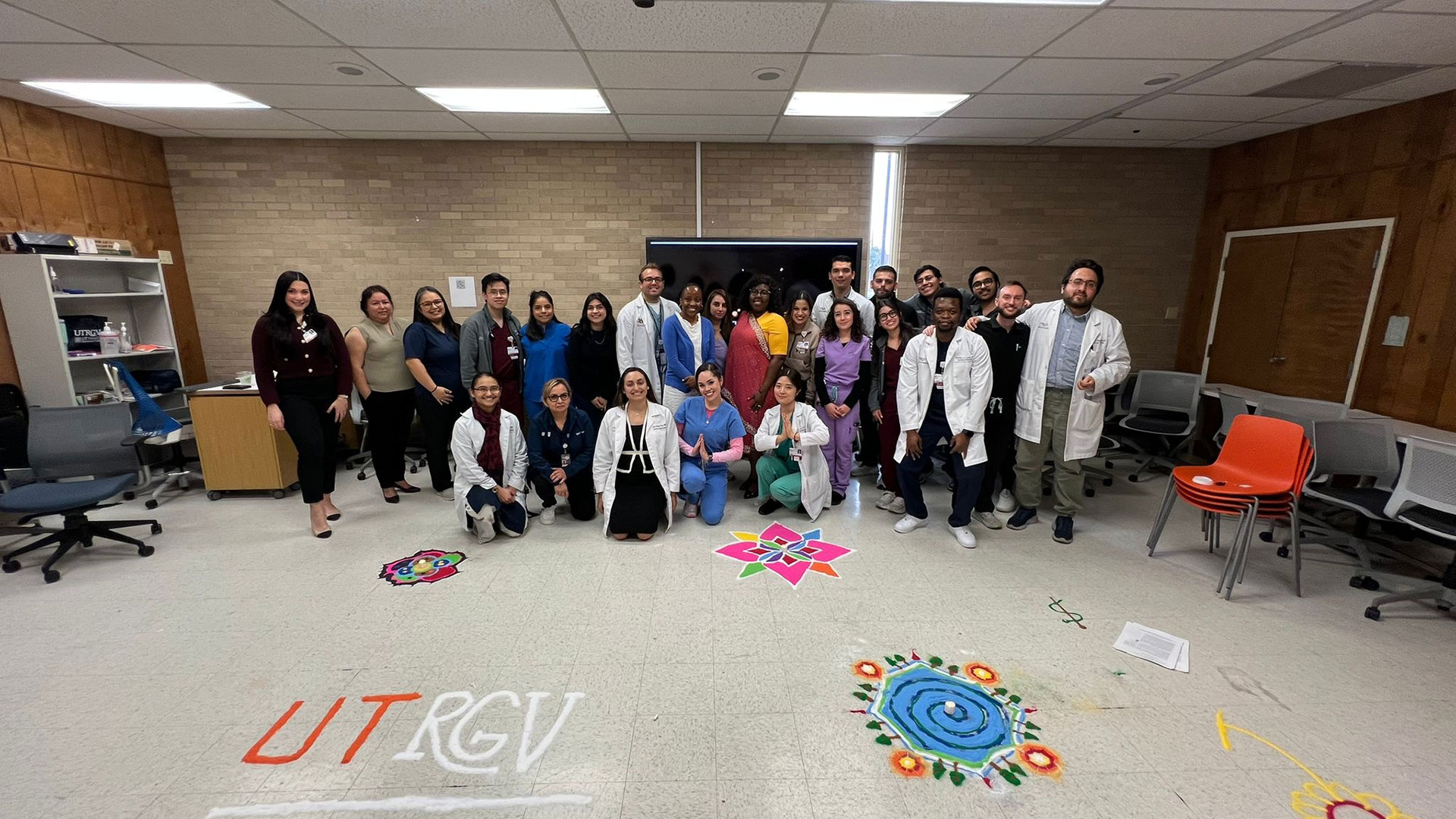 A large group of medical students and faculty pose for a photo in a classroom.