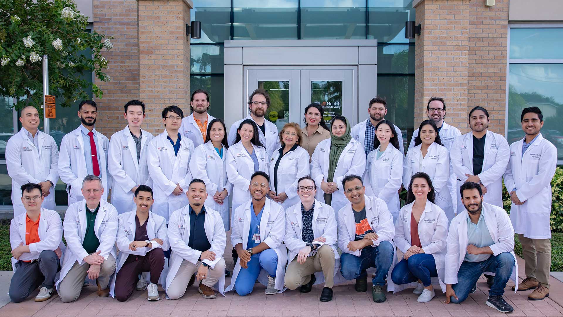 A group of medical professionals in white coats pose for a photo outside a building.