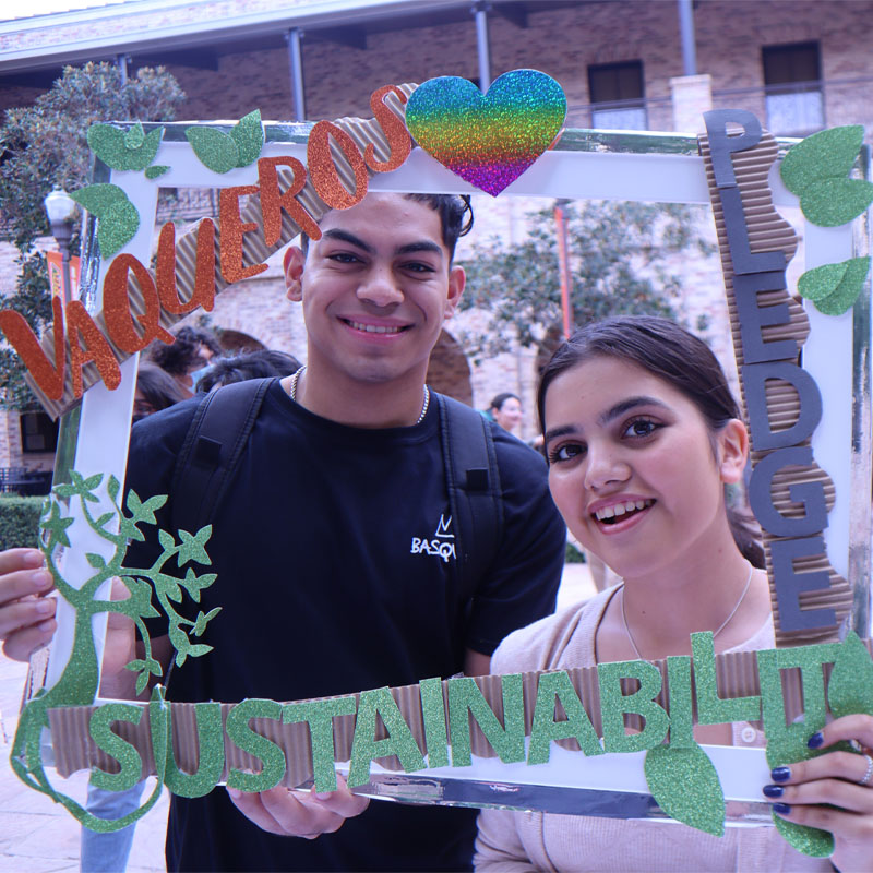 Two students on the Brownsville Campus taking a photo with the Sustainability Pledge selfie frame during Campus Sustainability Day hosted by the Office for Sustainability