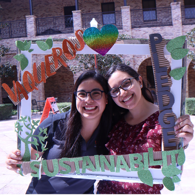 Two students on the Brownsville Campus taking a photo with the Sustainability Pledge selfie frame during Campus Sustainability Day hosted by the Office for Sustainability