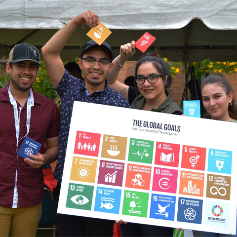 a photo of a group of students each holding an individual united nation goal image and one holding a big white sign of the 17 United Nation's Sustainable Development Goals