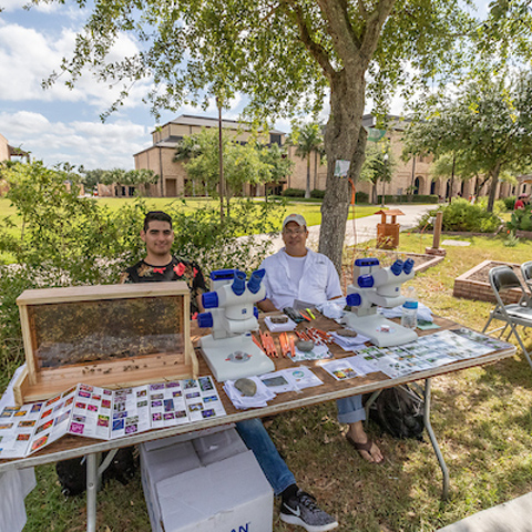 two men with a display table of different type of bees underneath a microscope and a bee hive on the table. Photo taken by David Pike