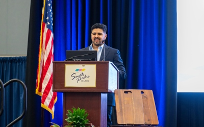 Jeremy San Miguel is speaking in front of an audience behind a podium that says South Padre Island