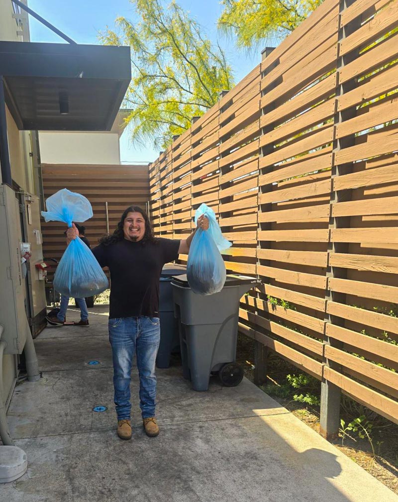 OFS Student Worker for Content Writing team Kevin Arevalo holding two bags of compost while smiling in backyard.