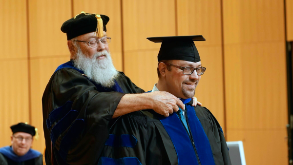 Dr. Bruce Reed, dissertation chair, places the hood over doctoral candidate Michael Herold during the inaugural Doctoral Hooding Ceremony at the Performing Arts Center on the Edinburg Campus. (UTRGV Photo by Jesús Alférez)