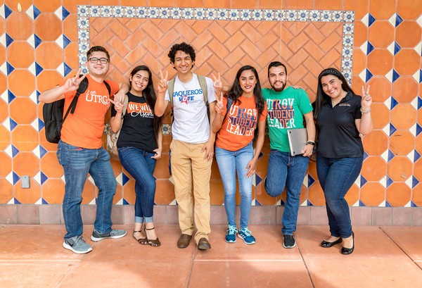 6 students with V's up in front of an orange wall at UTRGV. Photo taken by David Pike