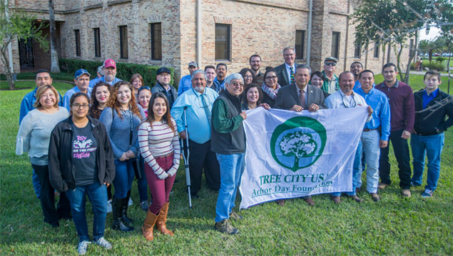 many UTRGV students, faculty, and staff infront of a big tree with people in the middle holding a tree campus usa designation banner at the Brownsville campus