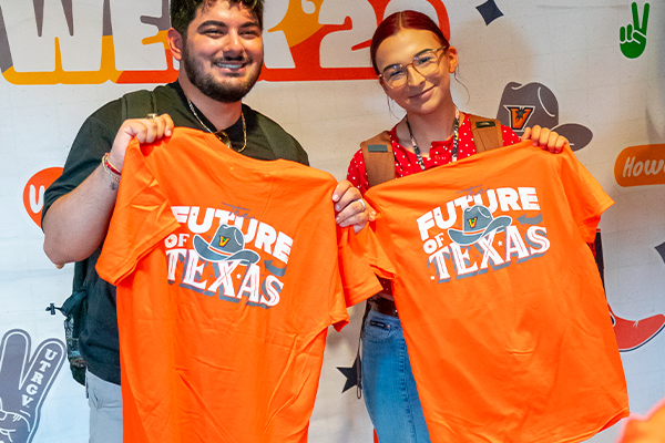 Photo of two people posing for a photo while holding orange UTRGV T-shirts.
